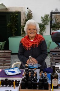 Mujer mayor sonriente vendiendo licor artesanal o Ginjinha en un mercado local de Lisboa