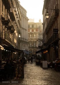 Calle del centro de Lisboa iluminada por el atardecer con gente en terrazas.