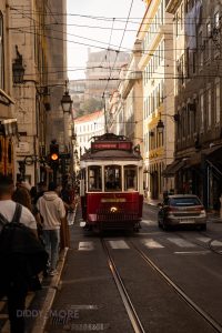 Tranvía 28 rojo circulando entre calles del centro histórico de Lisboa al atardecer