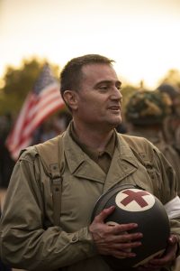 Militar estadounidense sonriendo junto a bandera americana en evento de recreación