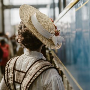 Mujer con sombrero vintage en estación de tren antigua – fotografía nostálgica de viaje en el Tren de la Fresa. 