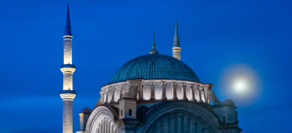Mezquita iluminada de Estambul al anochecer con cielo azul intenso y luna llena.