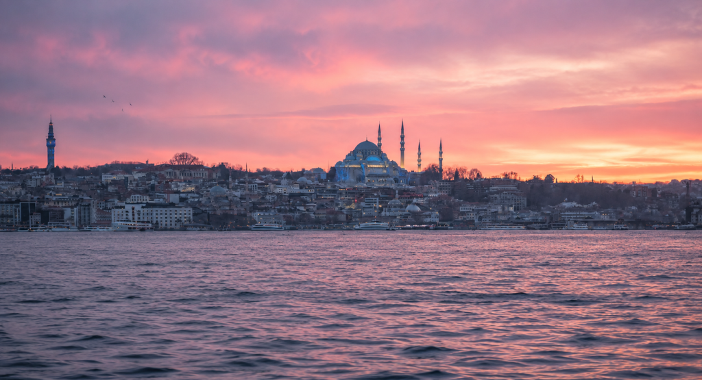Vista panorámica de la Mezquita de Süleymaniye en Estambul al atardecer, con tonos rosados y morados reflejados sobre las aguas del Cuerno de Oro.
