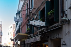 Fachada tradicional en Venecia con el cartel de Antica Casa Carettoni Locanda y flores en las ventanas. Si tu objetivo es viajar a Venecia, no te lo puedes perder.