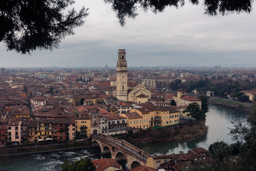 Panorámica de Verona con la catedral, el Puente de Piedra y el río Adigio al atardecer, capturada desde un mirador elevado.