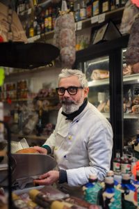 Hombre mayor con gafas y delantal blanco en tienda de productos típicos en Verona. Verona desde Venecia en un día.