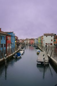 Barcas ancladas en un canal de Burano rodeado de casas de colores, en una excursión de Murano y Burano en un día.