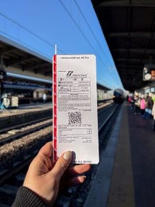Billete de tren Trenitalia de Venecia Mestre a Venezia Santa Lucia sostenido en el andén al sol de la mañana.
