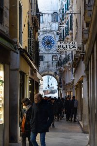 Callejón veneciano con luces y reloj astronómico al fondo