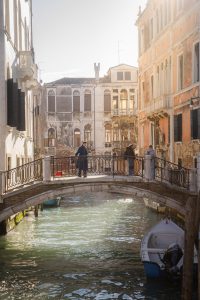 Puente veneciano iluminado por luz dorada al atardecer con reflejos sobre el canal y personas caminando