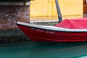 Primer plano de la barca roja “Nonno Giorgio” atracada en un canal de Burano, durante una ruta por Murano y Burano en un día.