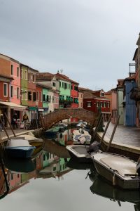 Canal con barcas y puente de ladrillo en Burano, rodeado de casas de colores, durante una excursión fotográfica a Murano y Burano en un día.